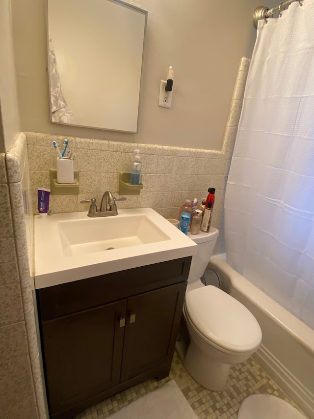 bathroom featuring toilet, a wainscoted wall, vanity, tile walls, and shower / tub combo with curtain