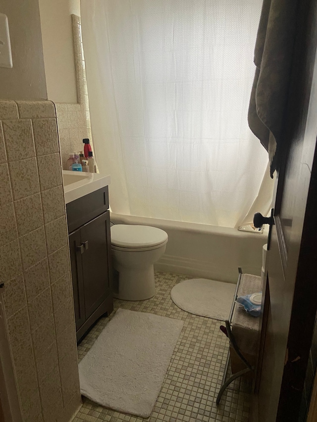 bathroom with toilet, tile patterned floors, shower / bath combo with shower curtain, vanity, and tile walls