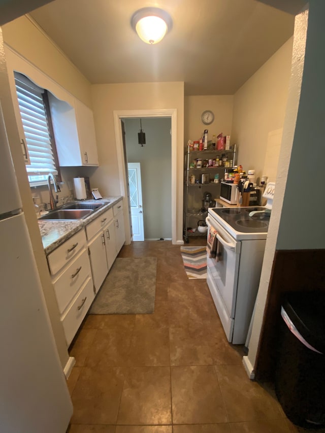 kitchen with white appliances, dark tile patterned floors, a sink, white cabinets, and light countertops