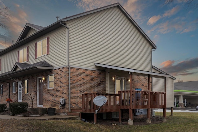 view of property exterior with a deck, a lawn, and brick siding