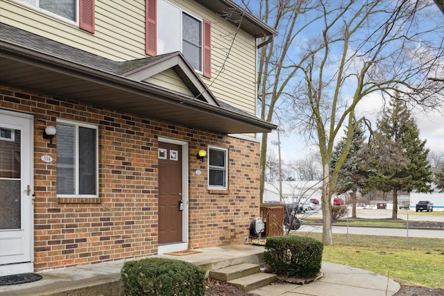 property entrance featuring brick siding and a shingled roof