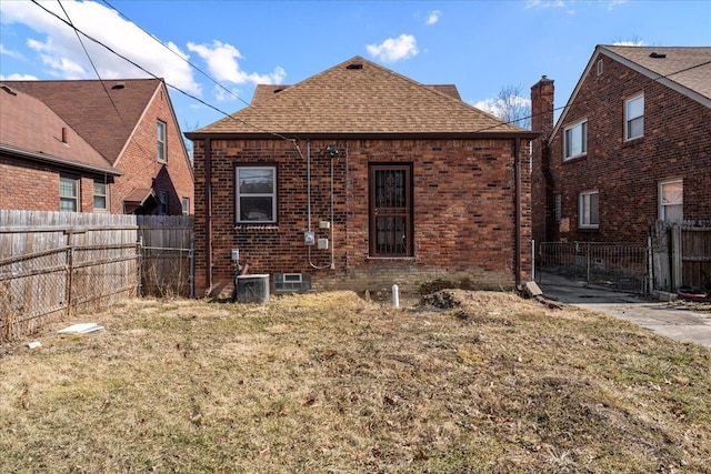 rear view of house with central AC, a fenced backyard, a yard, a shingled roof, and brick siding