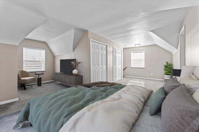 carpeted bedroom featuring baseboards, two closets, and lofted ceiling