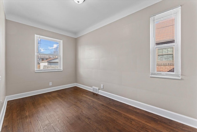 empty room featuring visible vents, dark wood-style floors, and baseboards