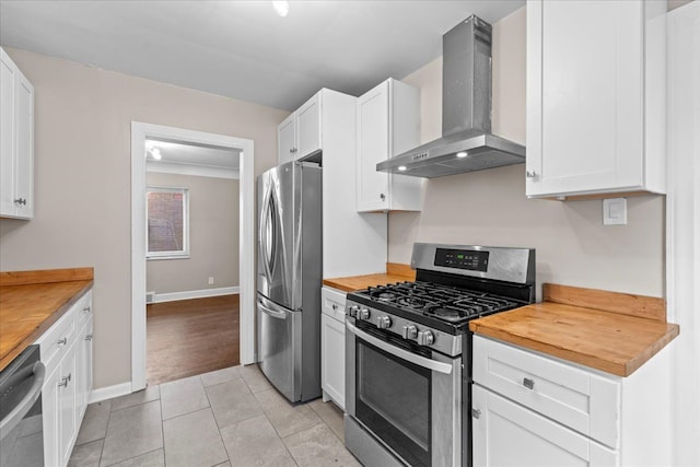 kitchen featuring stainless steel appliances, white cabinetry, wood counters, and wall chimney range hood