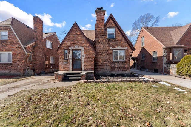 tudor home featuring brick siding, a chimney, and a front yard