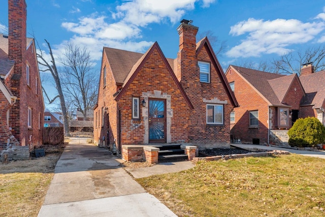 tudor home with a front lawn, brick siding, and a chimney