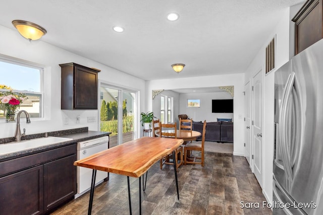 kitchen with a healthy amount of sunlight, dark brown cabinetry, white dishwasher, a sink, and stainless steel fridge