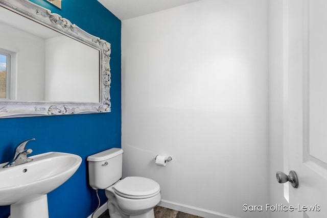 half bathroom featuring toilet, baseboards, a sink, and wood finished floors