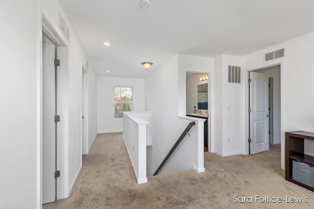 hall with light colored carpet, baseboards, visible vents, and an upstairs landing