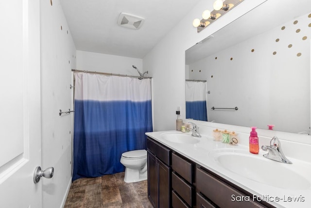 full bathroom featuring wood finished floors, a sink, toilet, and double vanity