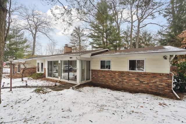 snow covered property featuring a sunroom, a chimney, and brick siding