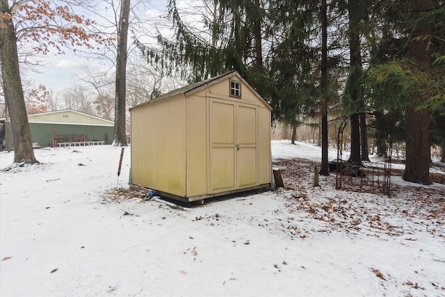 snow covered structure featuring an outbuilding and a storage unit