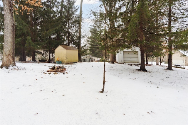 yard covered in snow featuring a garage, a storage shed, and an outdoor structure