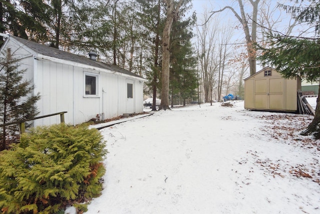 yard layered in snow featuring a shed and an outdoor structure