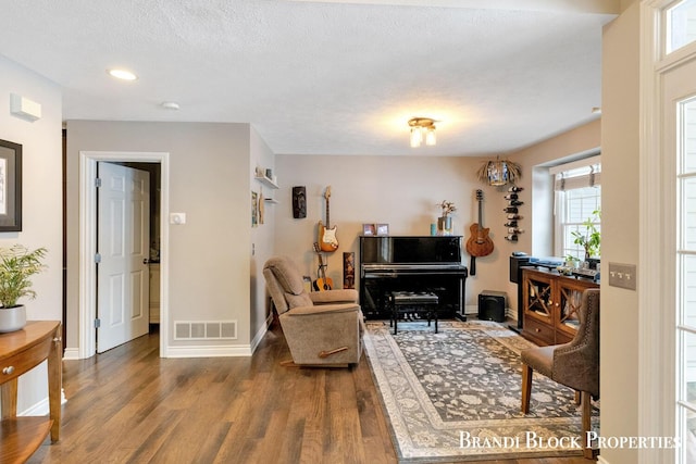 sitting room featuring dark wood-type flooring, visible vents, a textured ceiling, and baseboards