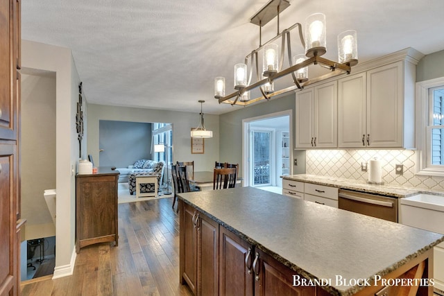 kitchen featuring a kitchen island, hanging light fixtures, stainless steel dishwasher, decorative backsplash, and dark wood finished floors