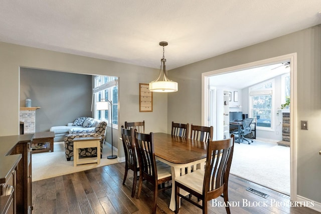 dining space featuring a brick fireplace, dark wood finished floors, and baseboards