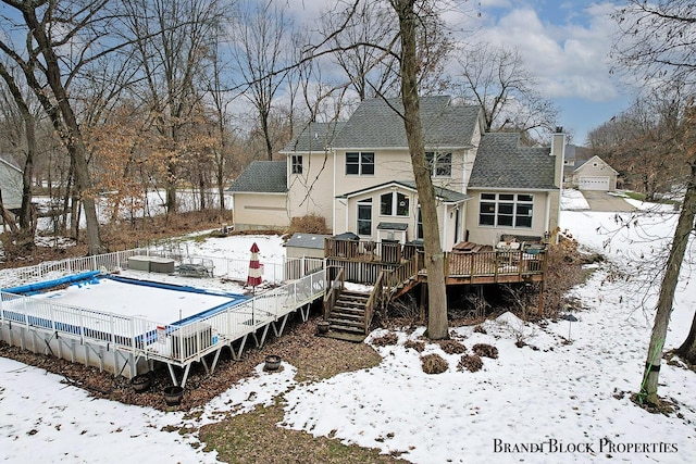 snow covered property with a garage, a fenced in pool, a fenced backyard, stairway, and a wooden deck