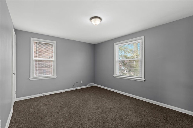 empty room with visible vents, baseboards, dark colored carpet, and a wealth of natural light