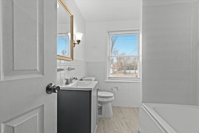 bathroom featuring toilet, a wainscoted wall, a bathing tub, vanity, and tile walls