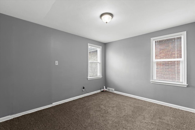 unfurnished room featuring visible vents, dark carpet, and baseboards