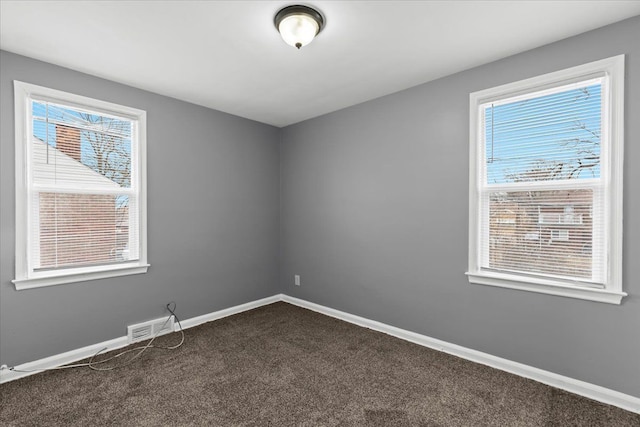 spare room featuring visible vents, baseboards, and dark colored carpet