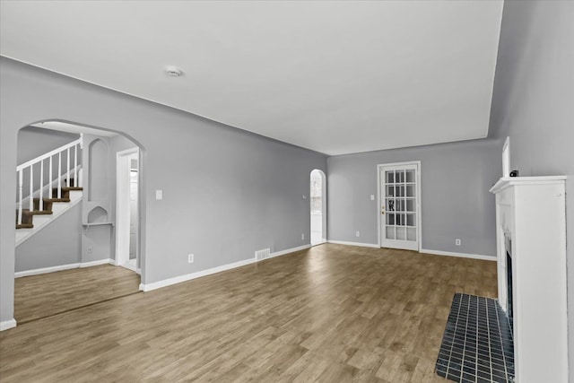 unfurnished living room with baseboards, visible vents, arched walkways, a fireplace with flush hearth, and wood finished floors