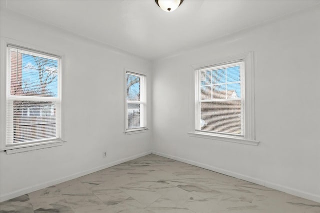 spare room featuring marble finish floor, plenty of natural light, and baseboards