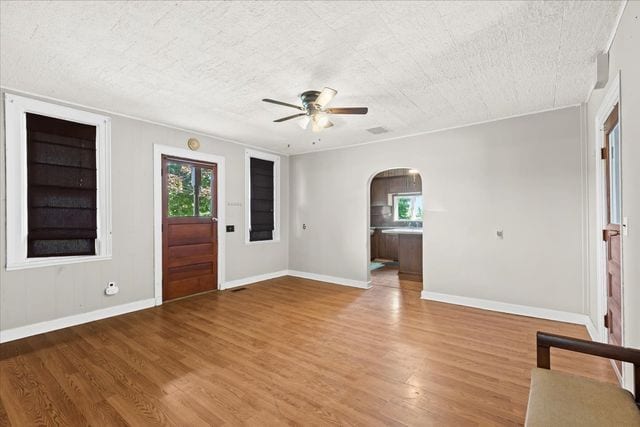 foyer with arched walkways, ceiling fan, light wood-style flooring, and baseboards