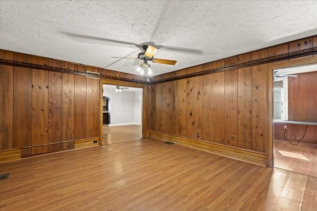 unfurnished room featuring a ceiling fan, wood walls, a textured ceiling, and wood finished floors