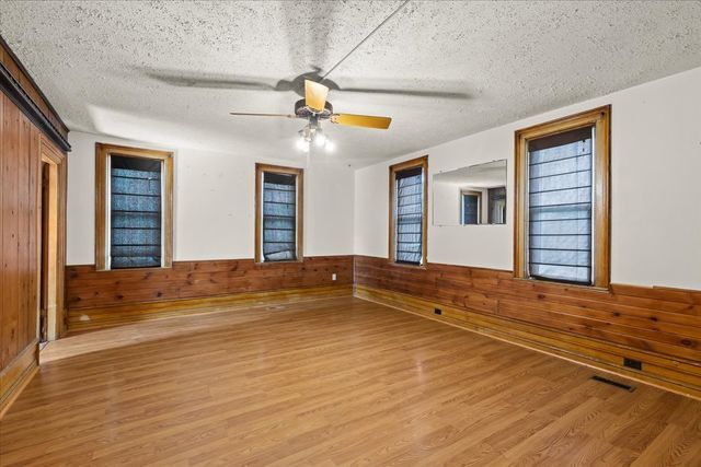 unfurnished room featuring a textured ceiling, a wainscoted wall, wood walls, a ceiling fan, and light wood-type flooring