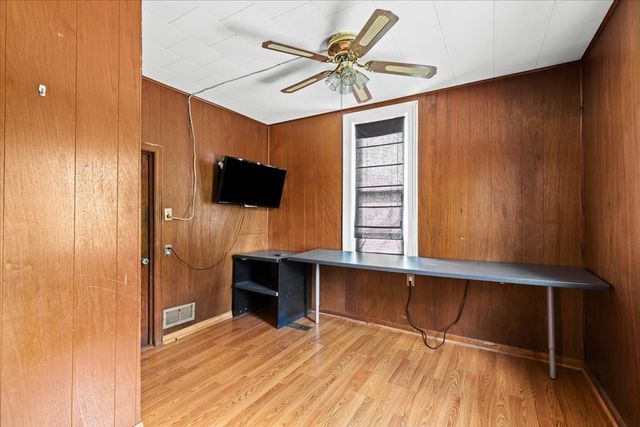 office space with ceiling fan, wood walls, wood finished floors, and visible vents