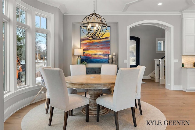 dining room featuring ornamental molding, arched walkways, baseboards, and light wood finished floors