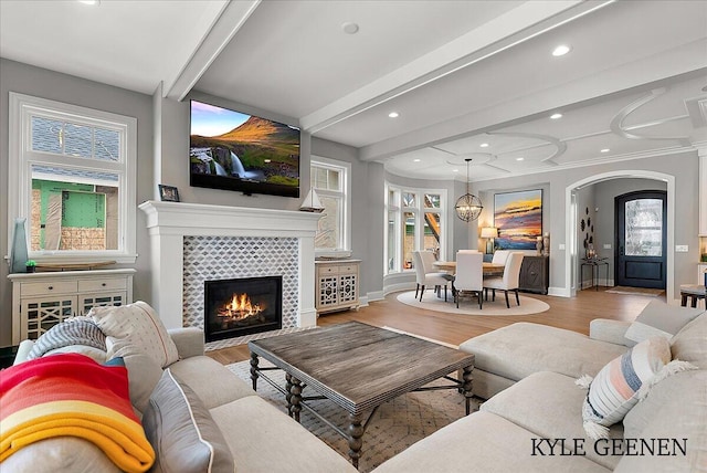 living room featuring arched walkways, beam ceiling, a fireplace, wood finished floors, and baseboards