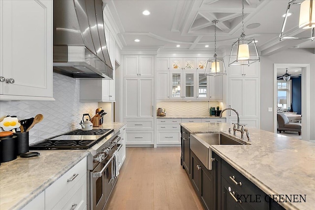 kitchen featuring coffered ceiling, wall chimney range hood, double oven range, white cabinetry, and a sink