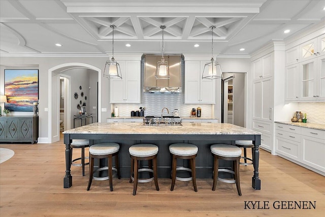 kitchen with arched walkways, white cabinets, wall chimney exhaust hood, a breakfast bar area, and light wood-type flooring