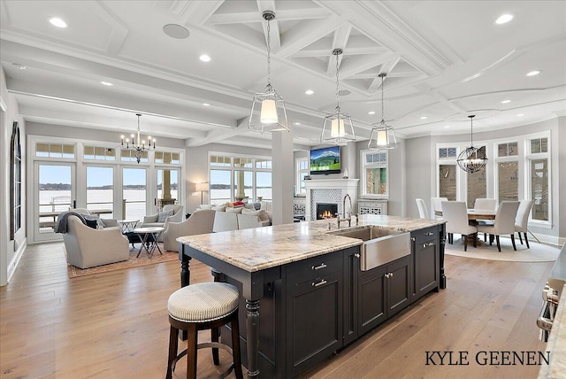 kitchen with a chandelier, a warm lit fireplace, a sink, and light wood-style flooring