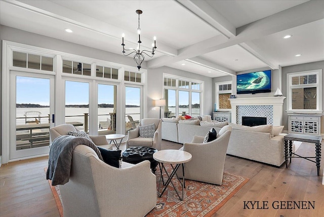 living room featuring light wood finished floors, a tiled fireplace, beamed ceiling, and recessed lighting