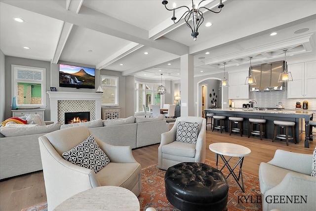 living room featuring arched walkways, a tile fireplace, coffered ceiling, wood finished floors, and an inviting chandelier