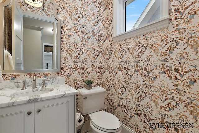 bathroom with vanity, toilet, and wallpapered walls