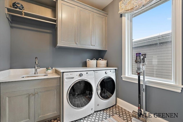 laundry room featuring washing machine and dryer, cabinet space, a sink, and baseboards