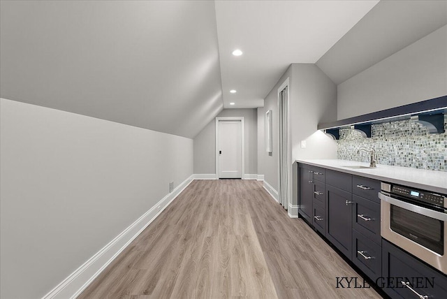 bar featuring a sink, stainless steel oven, baseboards, light wood-type flooring, and decorative backsplash