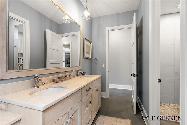 bathroom with a sink, a tile shower, baseboards, and double vanity