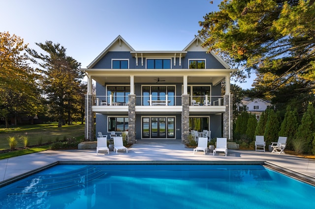 rear view of property featuring a ceiling fan, an outdoor pool, a patio, and a balcony