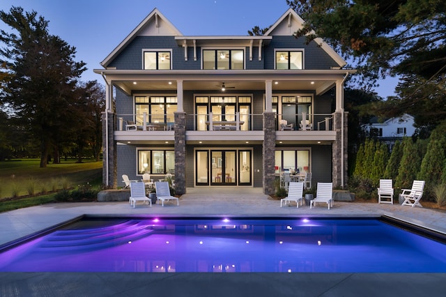 back of property with a balcony, a patio area, an outdoor pool, and a ceiling fan