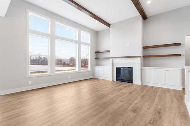 unfurnished living room with light wood-style floors, a glass covered fireplace, beamed ceiling, and baseboards