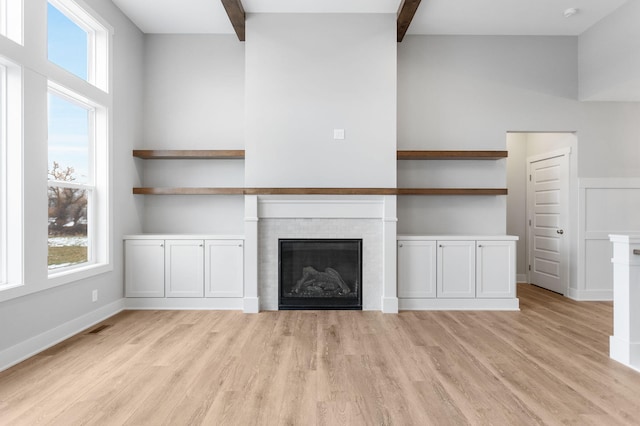 unfurnished living room with vaulted ceiling with beams, light wood finished floors, visible vents, a glass covered fireplace, and baseboards