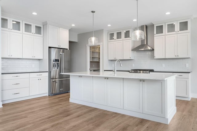 kitchen with light wood-style flooring, high end refrigerator, a sink, wall chimney exhaust hood, and a center island with sink