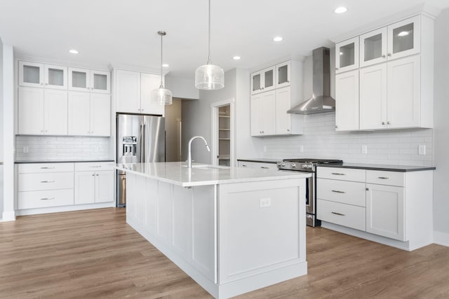 kitchen with a center island with sink, wall chimney exhaust hood, light wood-style flooring, appliances with stainless steel finishes, and a sink